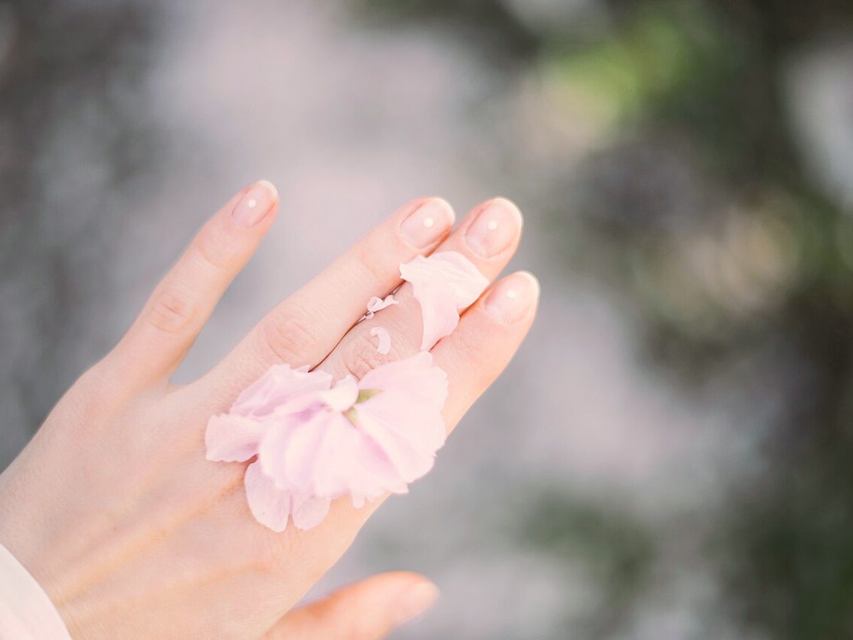 Main à la manucure nude et pétales de fleur